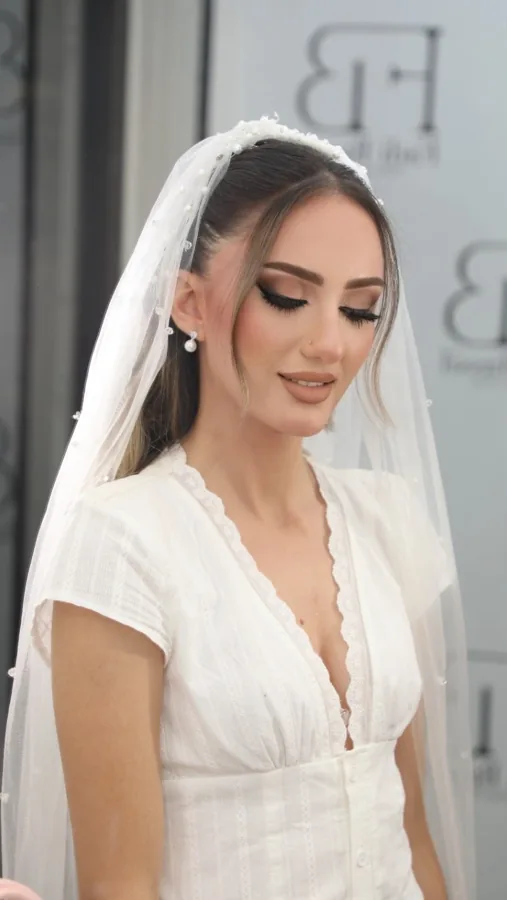 Soft bridal makeup with defined lashes and a nude lip beneath a white veil
